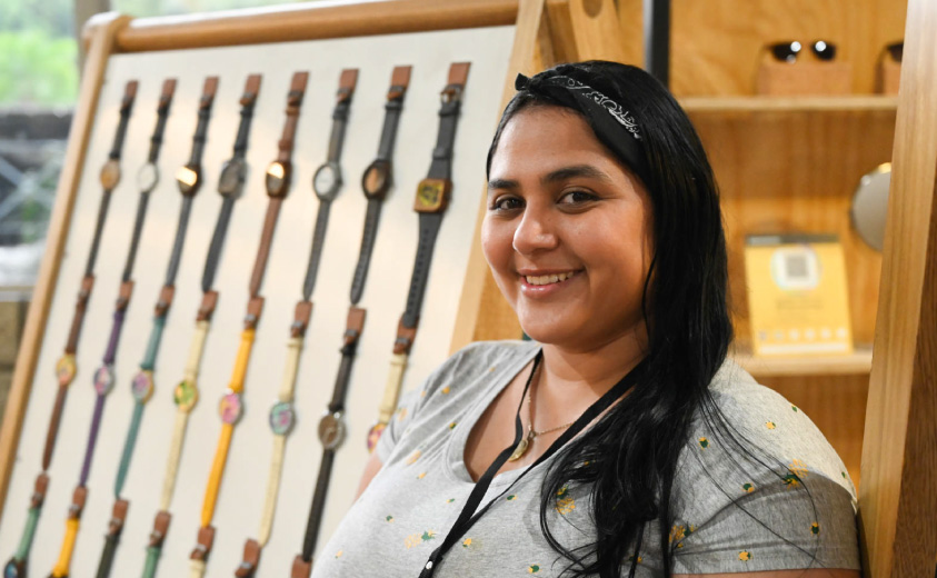 Foto de la artesana Melany Bolivar y al fondo, se ven los relojes artesanales que se elaboran en su taller