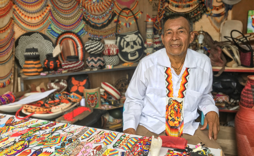 Fotografía del artesano José Flamedes Chirimía en un stand de feria con las artesanías elaboradas por su grupo Tai K'a.